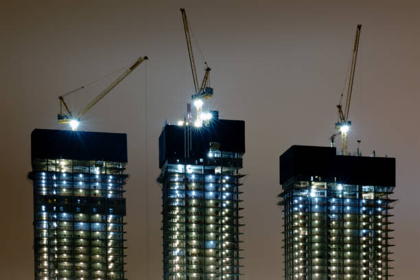 istock Construction of three high-rise buildings using cranes. Night construction of skyscrapers with floodlights 1203720972
