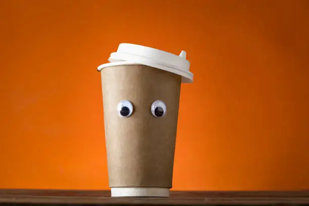Creative coffee cup with funny eye on a orange background