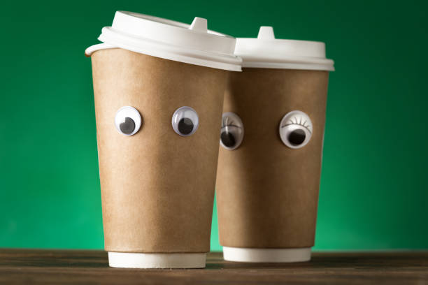 istock Creative two coffee cup with funny eye on a green background 1203722400