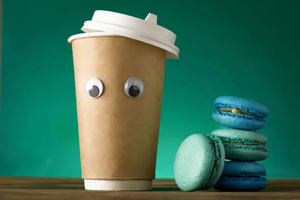 Creative coffee cup with funny eye and macaroon on a green background