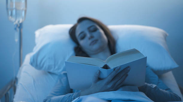 istock Young sleepless patient lying in the hospital bed and reading a book 1203723476