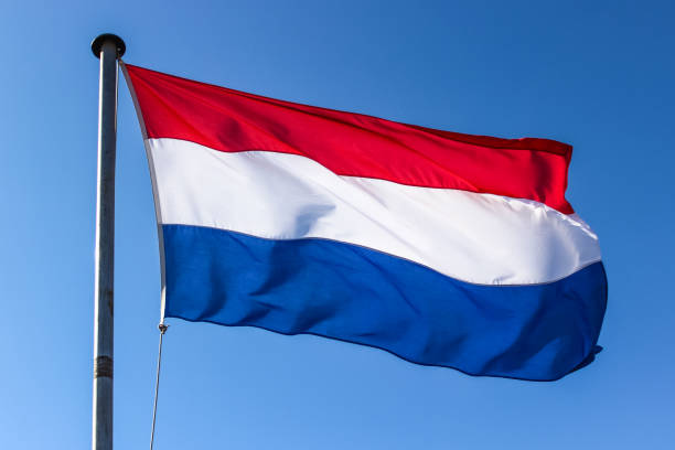 istock Dutch flag on a flagpole waving in the wind, close up on a blue sky background 1203723590