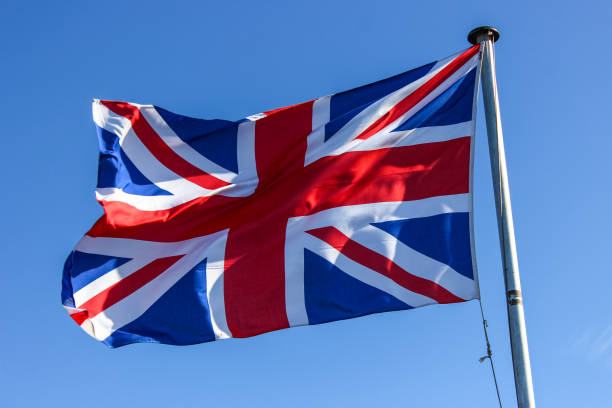 istock United Kingdom flag waving with a bright blue sky background 1203723614