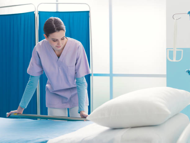 istock Young trainee nurse working at the hospital and adjusting bed rails 1203723716