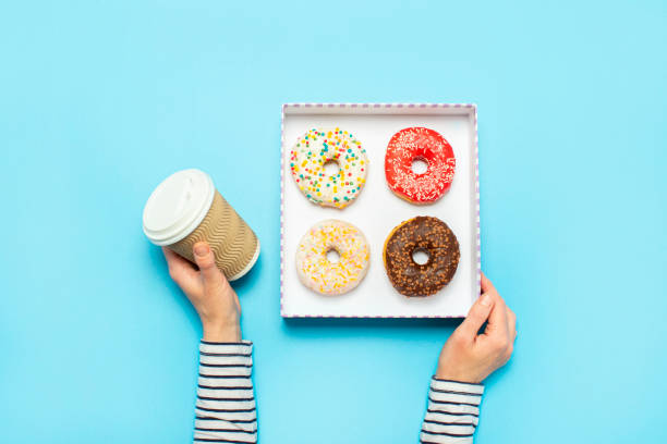 istock Female hands hold a box with donuts, a cup of coffee on a blue background. Concept confectionery store, pastries, coffee shop. Banner. Flat lay, top view 1203725017