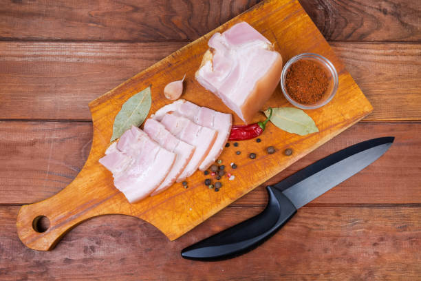 istock Sliced boiled-smoked pork belly, spices on cutting board, knife 1203726995