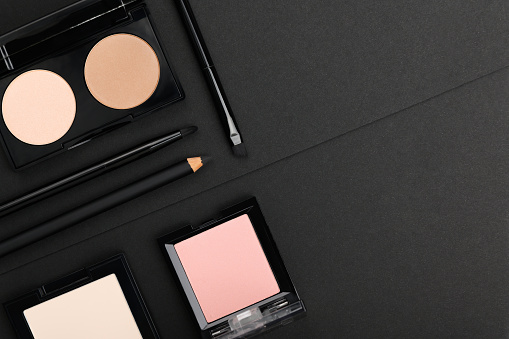 Make up products on black background. Powder, blush palettes, lipstick, eyeliner and brushes from above. Decorative cosmetics top view geometric backdrop. Female glamour professional beauty products