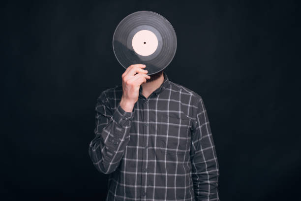 istock One man is covering his face with a record vinyl on black background. 1203731302