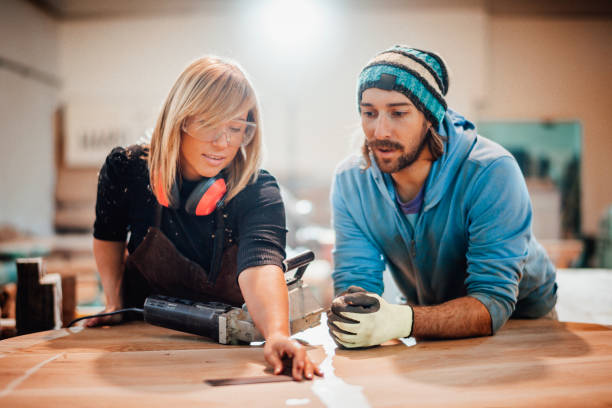 istock Two diverse carpenters evening out a wooden table surface together in a workshop 1203731767