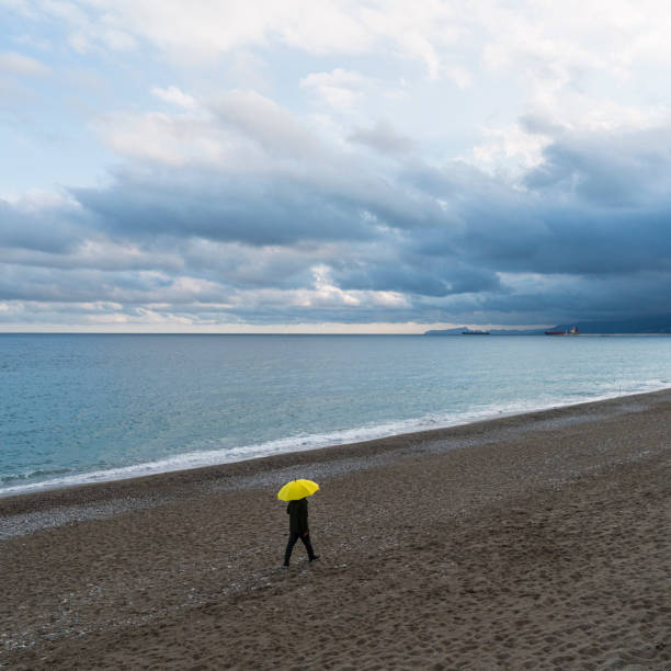 istock Lonely man walking on the beach on a rainy day 1203731776