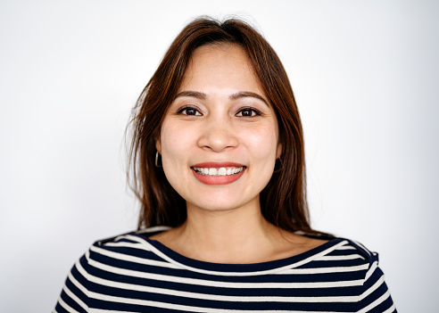Front view close-up of mid adult Chinese businesswoman with long brown hair wearing striped boatneck top and smiling at camera against white background.