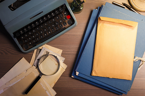 Investigator desk with confidential documents, magnifying glass, vintage typewriter. Secret documents investigation concept.