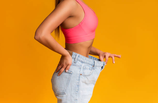 fit girl posing in oversize jeans over yellow background - torso women jeans abdomen imagens e fotografias de stock
