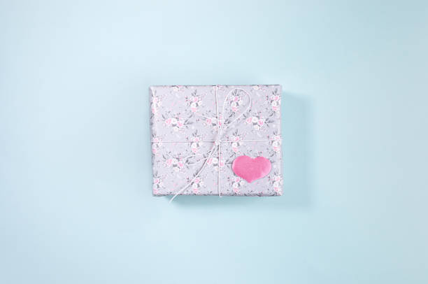 istock Gift box wrapped with grey paper with floral pattern and pink heart on light blue background. Valentine's day. 1203742843