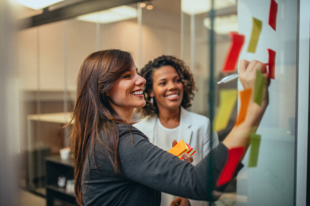 smiling businesswoman brainstorming with adhesive notes on a glass wall in the office. - team human hand cheerful close up imagens e fotografias de stock