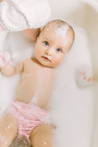 Happy laughing baby taking a bath playing with foam bubbles. Little child in a bathtub. Infant washing and bathing. Hygiene and care for young children. face of a little baby in the bathroom