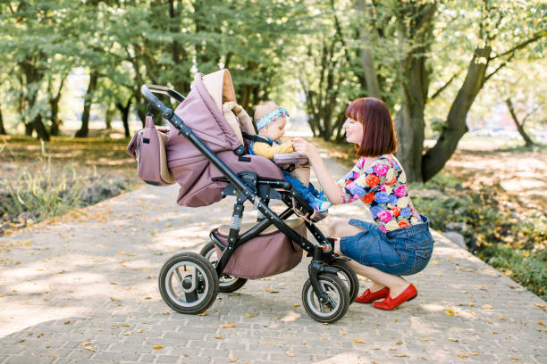 młoda matka patrząc na swoje dziecko w wózku dziecięcym - baby toddler young women outdoors zdjęcia i obrazy z banku zdjęć