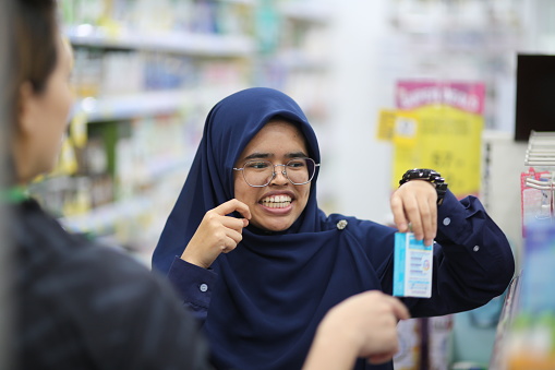 A Muslim female pharmacist is explaining supplement benefits to female customer in pharmacy.