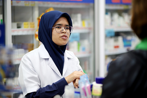 A Muslim female pharmacist is attending to female customer in pharmacy.