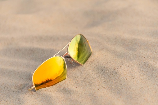 Sunglasses on beach reflecting sand dunes. Mirrored sunglasses on sandy beach in summer day. Sunglasses on sand as summertime vacation concept.