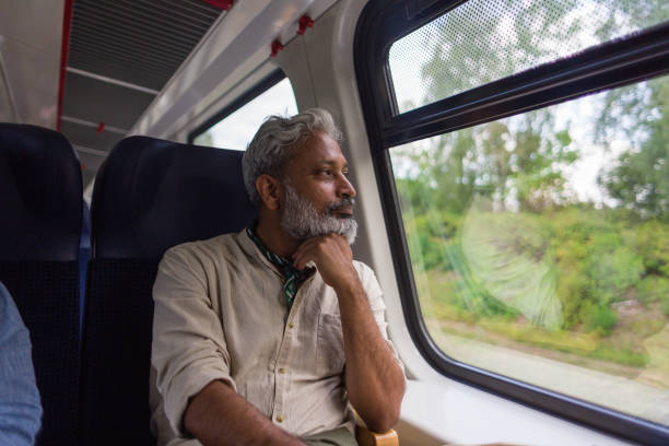 istock Indian mature man with hand on chin thinking about life while looking through train window 1203750700