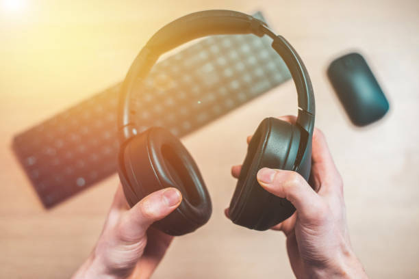 istock Workspace audio concept: Holding black wireless headphones, workspace in the blurry background 1203757307