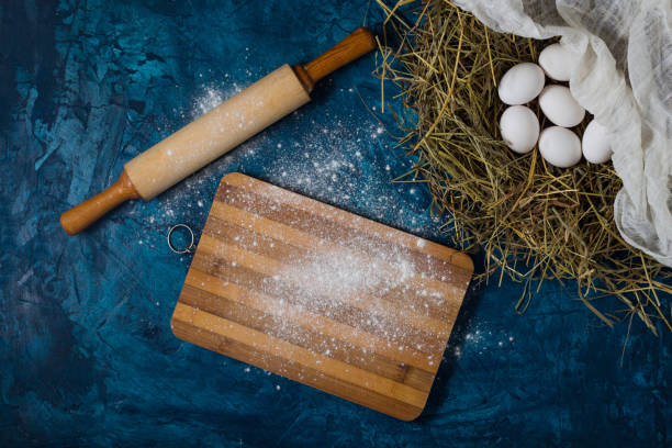 istock Eggs in the Nest, kitchen accessories, rolling pin, cutting board and scattered Flour on the Blue Background. Copy space. Flat lay, top view 1203757593