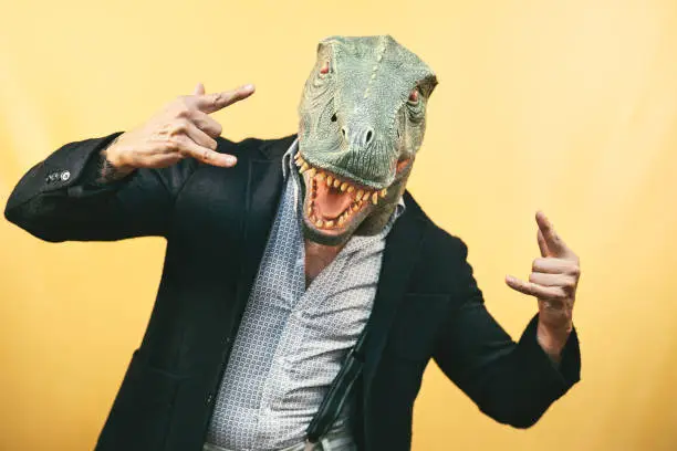 Senior man wearing t-rex dinosaur mask - Crazy hipster guy having fun celebrating carnival holidays - Absurd and surreal funny concept - Yellow background