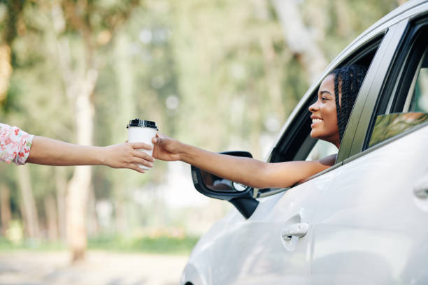 Driver buying morning coffee Happy pretty young Black woman buying coffee in drive through coffeeshop drive through photos stock pictures, royalty-free photos & images