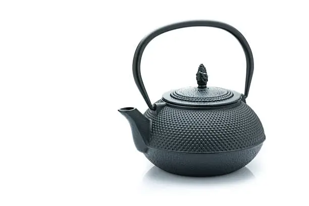 Black cast iron teapot isolated on reflective white background. The composition is at the right of an horizontal frame leaving useful copy space for text and/or logo at the left. Predominant colors are black and white. High resolution 42Mp studio digital capture taken with Sony A7rii and Sony FE 90mm f2.8 macro G OSS lens