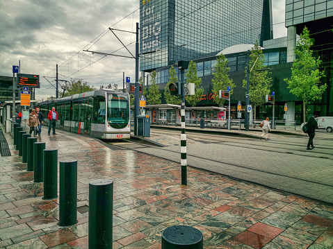 Rotterdam, Netherlands - August 9, 2019: Few people come off the train Citadis 302 which shuts the doors and ready to depart. The stop platform tiled with brown granite. The black steel poles bar the bicycles crossing the railways.