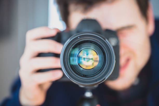istock Photographer at work: Man is standing behind a professional camera on a tripod, making pictures 1203771663