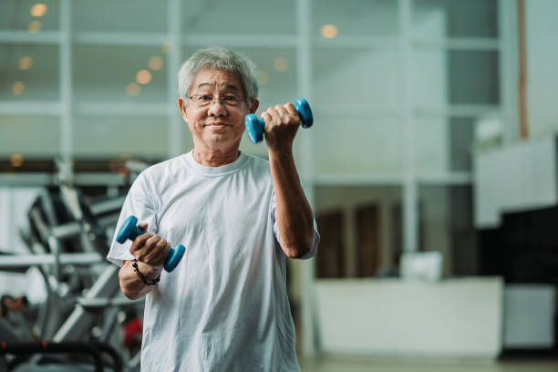 Asian chinese active senior male exercising and workout with dumbbell in gym room during weekend activity stock photo