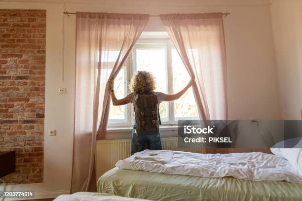 Rear View Of Tourist In The Hotel Room Pulling The Curtains To See The View Stock Photo - Download Image Now
