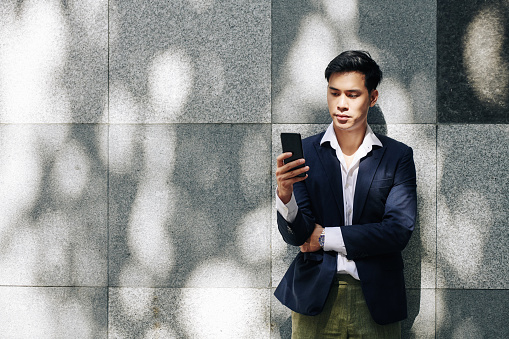 Pensive young handsome businessman reading text messages in his smartphone