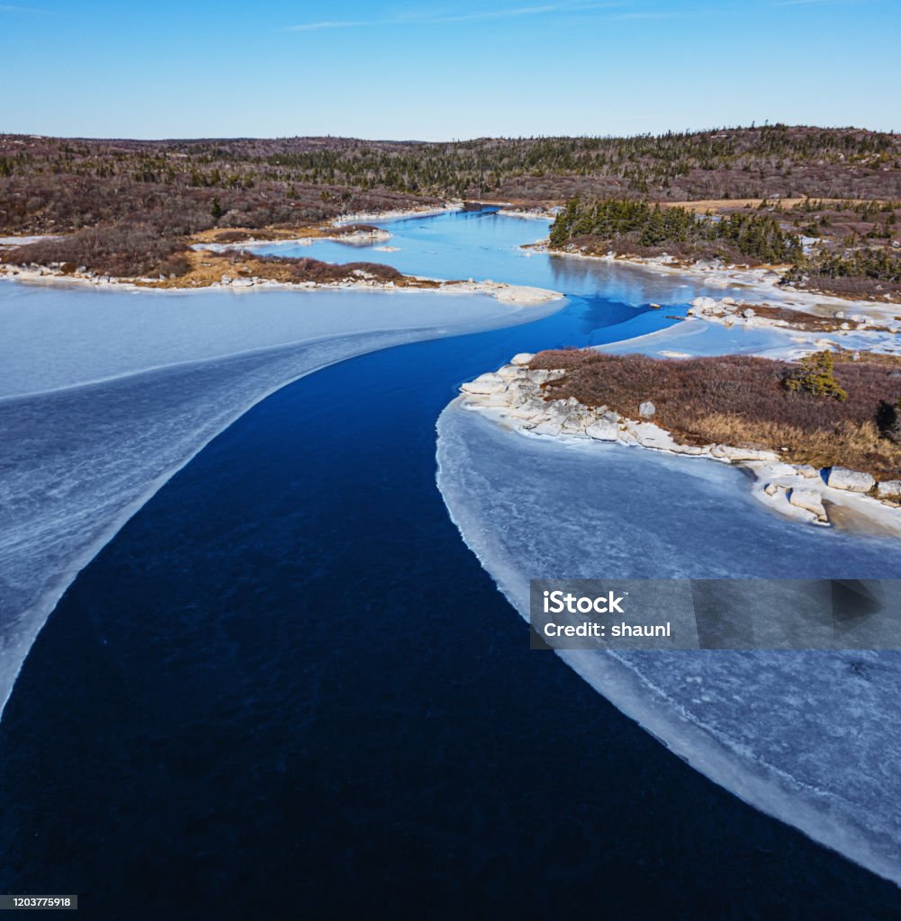 Tidal River Below Aerial drone view of a tidal river flowing toward the sea, surrounded by ice. Aerial View Stock Photo