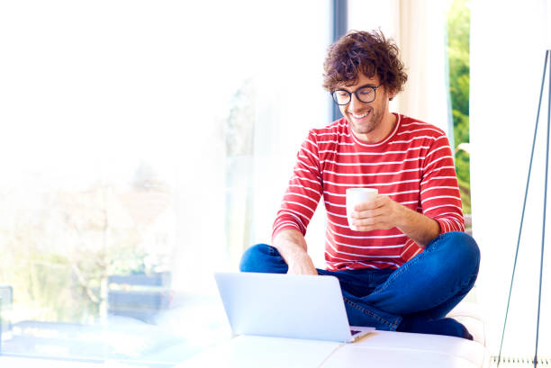 istock Handsome and happy young man using his laptop while relaxing at home 1203778837