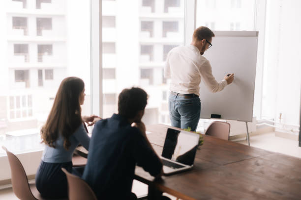 istock Young confident businessman presenting new project to partners on whiteboard 1203780382