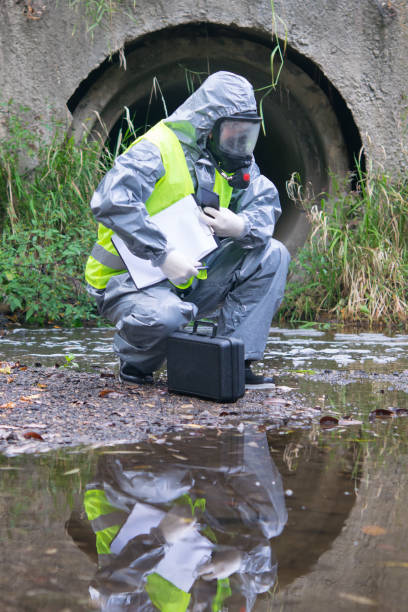 istock a specialist in a protective suit and mask, on the pond with a suitcase, tablet and mobile phone in his hands, conducts research 1203781332