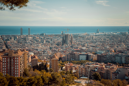 Breathtaking Barcelona city view at sunset from MUHBA Turó de la Rovira hill viewpoint, a must-visit destination offering panoramic vistas of the vibrant city below. Witness the captivating skyline as the sun dips below the horizon with a sea view, casting a warm glow over the architectural wonders and bustling streets of Barça and La Sagra da Familia in Catalonia, Spain. Don't miss the opportunity to capture stunning photographs of this iconic cityscape during the golden hour atop this historic vantage point. Barcelona's Grid pattern is breathtaking from above, making it one of the most beautiful cities globally, with the Sagrada Familia Cathedral as its crown.