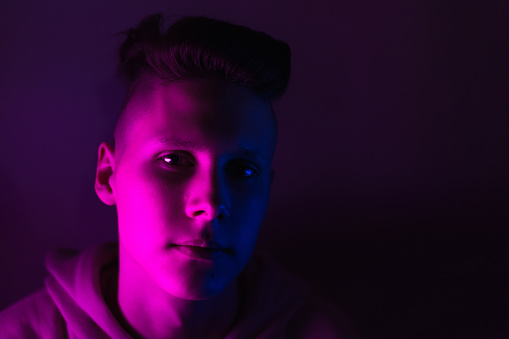 Young guy in a neon light. A teenager in a pink hoodie in trendy lighting of pink, purple and blue.