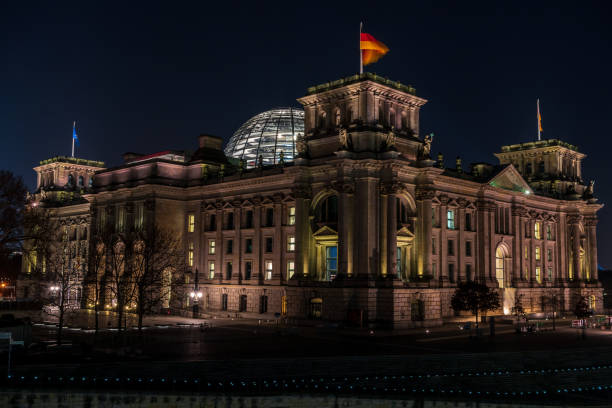the illuminated  Berlin Reichstag at night with lights of cars in the foreground