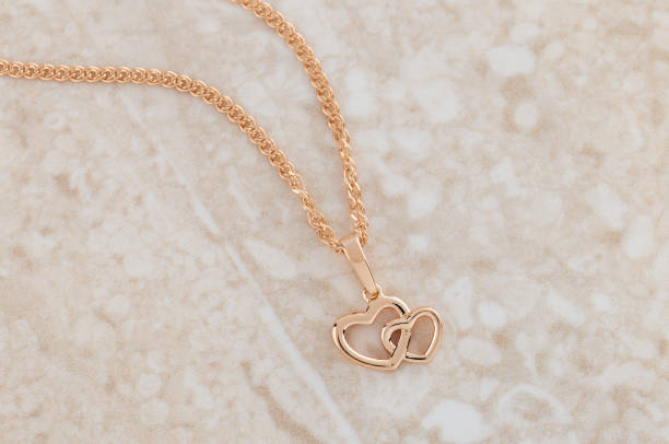 Hearts shape rose gold pendant necklace on beige marble background. Romantic  jewelry. Advertising still life product concept for Valentines Day