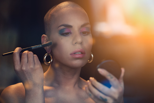 Bald headed girl applying colourful make-up.