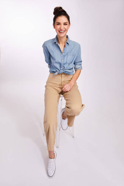 istock Laughing young brunette woman sitting on a stool on gray 1203787725