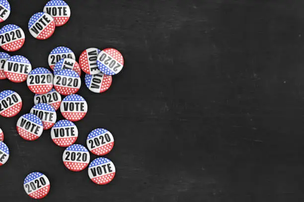 Large group of 2020 US presidential election pins on rustic black wood background with copy space.