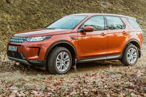 Moscow, Russia - December 20, 2019: side View of all new premium england suv. Land rover Discovery sport parked in the forest. Orange all wheel drive car standed on the ground.