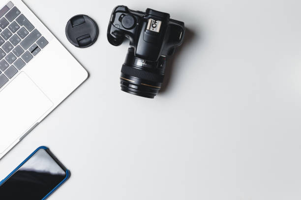 istock Photographer's workplace on a white background. Modern laptop, digital camera, lens, battery, smartphone. Minimalism. Top view. Copy space. Equipment for the photographer. The concept of freelancing 1203798703