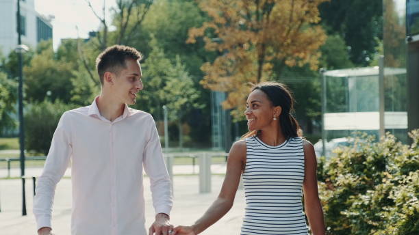 istock Multi-ethnic couple shyly looking at each other while walking the street 1203801781