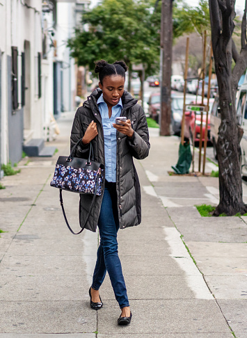 A woman concentrating on her phone as she slowly walks on a sidewalk in San Francisco, California.